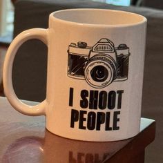 a white coffee mug with the words i shoot people on it sitting on a table