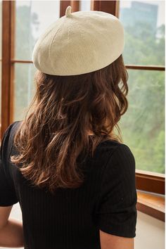 a woman with long hair wearing a white hat looking out the window at trees outside