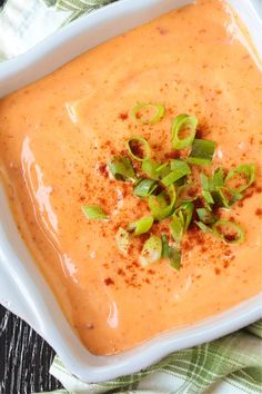 a square white bowl filled with soup and topped with green onion sprinkles