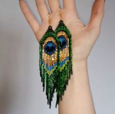 a woman's hand holding up a pair of beaded earrings with peacocks on them