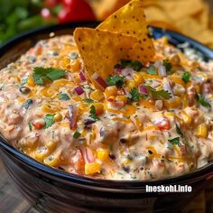 a black bowl filled with corn and salsa dip surrounded by tortilla chips on the side