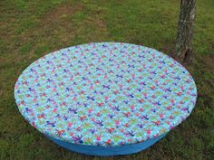 a blue and white flowered cloth covered table in the grass next to a tree