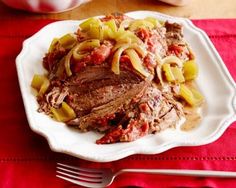 a white plate topped with meat and pasta covered in sauce on top of a red table cloth