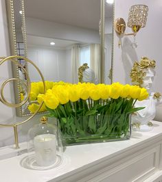 a vase filled with yellow flowers sitting on top of a white mantle next to a mirror