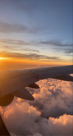 the wing of an airplane as it flies through the sky above clouds at sunset or dawn