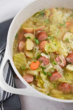 a white bowl filled with cabbage and sausage soup on top of a blue towel next to a black and white striped napkin