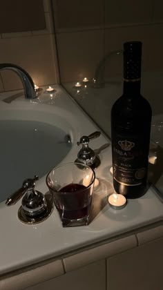 a bottle of wine sitting on top of a bath tub next to a glass filled with liquid