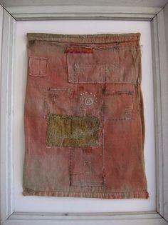 an old piece of cloth is hanging in a white frame with a red and yellow patch on it