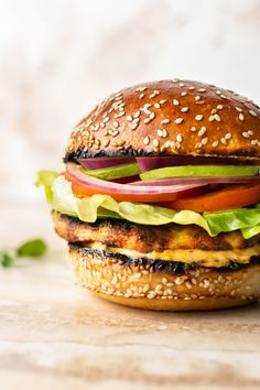 a chicken burger with lettuce, tomato and onion on a sesame seed bun