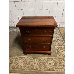 a wooden dresser sitting on top of a rug next to a brick wall and floor