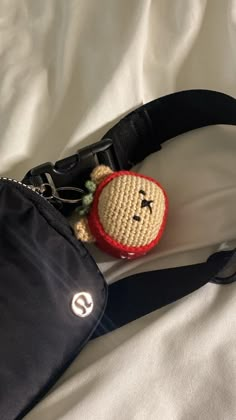 a small crocheted teddy bear in a black purse on a white bed sheet