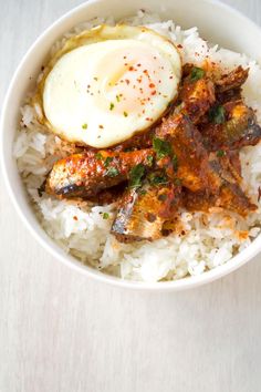 a white bowl filled with rice and meat covered in an egg on top of it