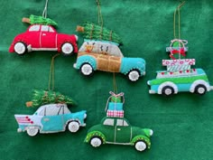 four ornaments are hanging on a green cloth covered tablecloth with cars and christmas tree decorations