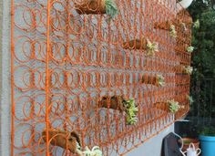 an orange wire fence with plants growing on it and hanging from the side of a building