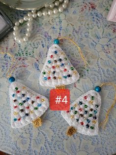 three crocheted christmas trees on a table next to pearls and a cell phone