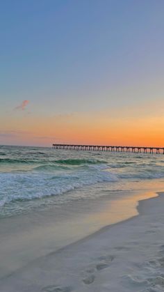 the sun is setting over the ocean with a long pier in the distance and waves crashing on the beach