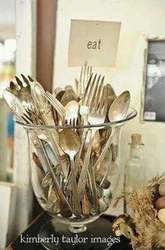 a glass bowl filled with lots of silverware on top of a table next to eggs