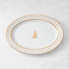 a white and gold plate with a small christmas tree on the rim, sitting on a marble surface