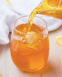 a pitcher pouring orange juice into a glass filled with ice and lemon slices on a wooden table