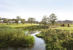 a small river running through a lush green field next to a wooden bridge over water