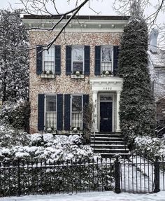 a large brick house with black shutters and snow on the ground in front of it