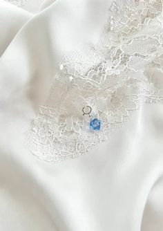 an image of white fabric with lace and blue stone brooch on it's lapel