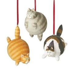 three ornaments in the shape of cats and a cat on one ornament are hanging from red strings