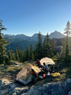 two tents set up on the side of a mountain with mountains in the background and trees around them