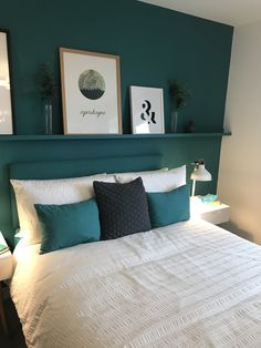 a bed with white sheets and pillows in a bedroom next to two framed pictures on the wall