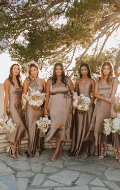 a group of women standing next to each other holding bouquets in front of a tree