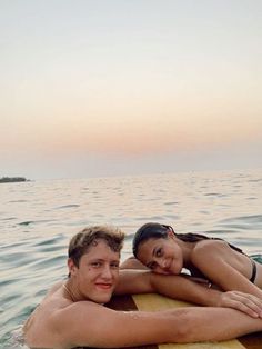 a man and woman laying on a surfboard in the middle of the ocean at sunset