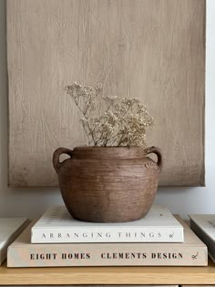 a wooden bowl with flowers sitting on top of three books in front of a painting