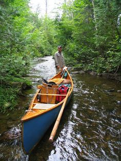 a man standing on the side of a river next to a blue and yellow canoe