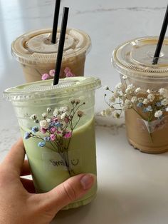 three iced drinks with flowers in them are being held by a person's hand