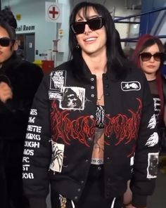 a man with black hair and sunglasses standing in front of other people wearing black clothing