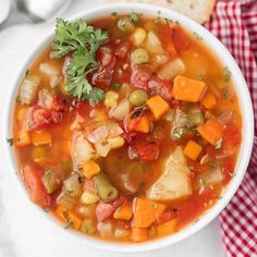 a white bowl filled with vegetable soup on top of a red and white checkered napkin