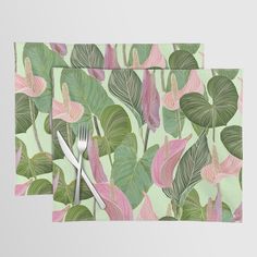 two placemats with pink and green leaves on them, one has a fork