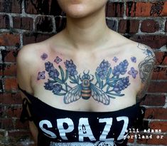 a woman with tattoos on her chest is wearing a black top and has purple flowers