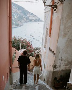 two people are walking down the stairs in front of an ocean and buildings with flowers on them