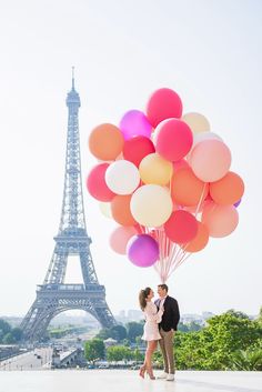 a man and woman kissing in front of the eiffel tower with colorful balloons