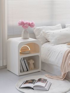 a bed with white sheets and pillows next to a book shelf filled with books on top of a round rug