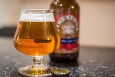 a glass filled with beer sitting on top of a table next to an empty bottle