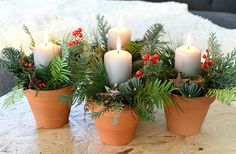 candles are lit in clay pots with greenery and berries on the table next to them