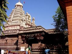 people are walking around in front of an ornate building that is surrounded by trees and bushes