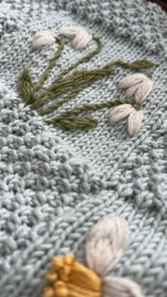 a close up of a knitted object with white flowers on it and green stems