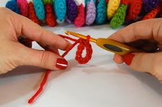 two hands are crocheting together with red yarn and orange crochet hooks