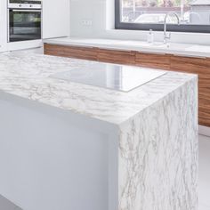 a white kitchen with marble counter tops and wooden cabinetry, along with an island