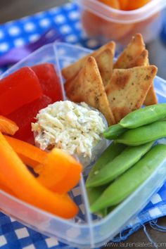 a plastic container filled with vegetables and crackers on top of a blue checkered table cloth