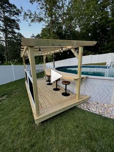 a wooden gazebo sitting on top of a lush green field next to a swimming pool