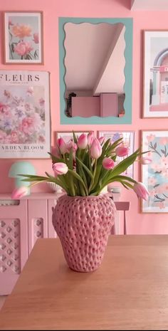 a vase filled with pink flowers sitting on top of a wooden table next to pictures